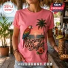 Pink t-shirt with Jimmy Buffett script text, a colorful parrot, palm tree, sunset beach scene, and tropical hibiscus flower.!