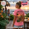 Woman wearing pink t-shirt with Jimmy Buffett graphic, palm tree sunset scene, and text reading It’s 5 O'clock Somewhere.!