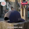 Navy blue baseball cap with embroidered XX logo on the side, metal buckle strap, resting on a concrete block outdoors.!