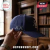 Navy blue baseball cap with embroidered grey cross eye icons on the side and LA logo on front against a library background.!