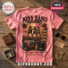 Pink t-shirt with Kiss band graphic, tropical concert illustration, guitar, and song titles on wooden surface background.!