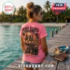 Woman wearing a bright pink KISS band graphic t-shirt featuring tropical concert artwork and song titles on a pier.!