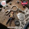 Kyle Busch metal keychain with miniature driver figure, racing tire, trophy charm, and shield text on wood background.!