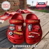 Red Liverpool FC themed slip-on clogs featuring team emblems, trophies, a jersey, and YNWA text on a wooden surface.!