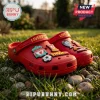 Red foam clogs with Liverpool FC branding, football charms, YNWA text, and club crests sitting on green grass and stones.!