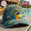 Margaritaville Jimmy Parrot Premium Embroidered Distressed Cap in teal with tropical patches on a wooden deck background.