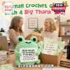 Light green crochet frog plush holding a sign that reads Never fro-get the difference you make with an office background.!