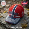 Red baseball cap with blue bill, white geometric patterns, Norway text, and compass graphic on a rocky outdoor surface.!