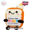Crocheted toast plush toy with orange crust, cream face, black bead eyes, and a small yellow-topped winter hat.!