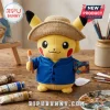Pikachu plush wearing a straw hat and blue artist shirt holding a paintbrush and palette on a wood table with paint tubes.!