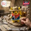 Pikachu plush toy wearing a tan safari hat and blue vest holding a small silver pickaxe in a miniature cave setting.!