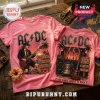Pink cotton t-shirt featuring AC/DC graphics, Angus Young, electric guitars, and song titles on a rustic wooden background.!