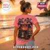 Pink t-shirt with AC/DC concert graphic featuring a bell, lightning, and song titles on a woman at a beach sunset.!