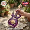 Purple glass guitar-shaped bottle with gold hardware and Prince symbol, held by a hand on a wooden table outdoors.!