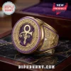 Gold championship-style ring featuring Prince's love symbol, purple enamel, and guitar engravings on a wooden base.!
