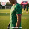 Man wearing a green soccer jersey with Aztec patterns and a Mexico national team crest on a grass field.!