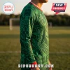 Green long-sleeve soccer jersey with black Aztec-inspired patterns and red cuffs on a person at a sports field.!