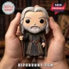 Gandalf vinyl figure with grey hair, beard, staff, and hooded cloak held in hands against a blurred library background.!