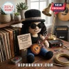 Crochet Slash doll wearing black hat and sunglasses, holding a miniature sunburst electric guitar on a wooden desk.!