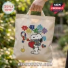 Beige canvas tote bag featuring an embroidered Snoopy holding a heart and flowers with colorful autism puzzle pieces.!