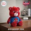 Superhero Bear Plush Doll in red and blue with spiderweb patterns, white muzzle, and large black eyes on a wooden desk.