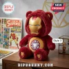 Superhero Bear Plush Doll featuring an Iron Man gold mask and red fur hood sitting on a wooden desk near comic books.