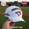 Toronto Blue Jays EST 1977 white cap with blue embroidery, featuring a jay bird logo and baseball diamond background.