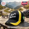 Black and yellow Tour de France baseball cap with white embroidered text, sitting on a wooden table near mountain roads.!