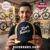 Man holding a black and yellow Tour de France baseball cap with white embroidered text in a professional cycling shop.!