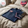 Navy blue USA soccer jersey with gold eagle graphic, American flag patch, and gold stripes on sleeves lying on a bed.!