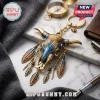 Western Bull Skull Boho Feather Keychain in metallic gold, blue, and orange tones resting on a marble and grey fabric surface.