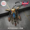 Western Bull Skull Boho Feather Keychain with blue and gold enamel detailing hanging against a gray concrete background.
