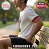 Man wearing a white waffle-knit ringer t-shirt with red trim and a colorful abstract graphic sitting on a wooden bench.!