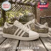 Adidas New Orleans Saints Who Dat Nation casual shoes in cream with gold team graphics on a rustic wooden table.