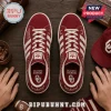 Adidas Oklahoma Sooners Suede Casual Sneakers in maroon with white stripes, team logos, and white laces on wood surface.