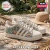 Adidas x The Golden Girls casual sneakers in cream with teal tropical print, cheesecake graphics, and classic text branding.