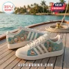 Adidas x The Golden Girls Casual Sneakers with pastel blue, palm tree, and character graphics on a wooden boat deck.