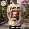 Cobra Kai Strike First Strike Hard cream t-shirt featuring Snoopy in a karate gi against a red sun and bamboo graphic.