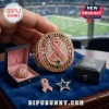Dallas Cowboys Breast Cancer Awareness Ring featuring a pink ribbon, gold metal, and crystal accents on a blue velvet stand.