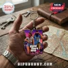 Grand Theft Auto VI Vice City keychain featuring a purple VI logo and the game protagonists held in a hand over a desk.