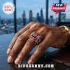 Omega Psi Phi Purple Amethyst Gold Ring featuring fraternity crest on a finger against a blurred city skyline background.