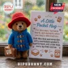 Paddington Bear needle felted pocket hug wearing a red hat and blue coat, holding a suitcase next to a printed card.