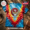 San Francisco 49ers x Grateful Dead mascot shirt with red, yellow, and blue tie-dye pattern on a wooden background.