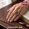 The Chosen 7th Anniversary Crystal Ring featuring a round green face and gold band worn on a finger over an open Bible.