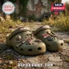 The Walking Dead Olive Green Clogs with Charms featuring a miniature sheriff hat, katana, crossbow, and baseball bat designs.