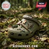 The Walking Dead Olive Green Clogs with Charms featuring a baseball bat, Terminus sign, and walker head on a forest floor.
