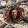 Tim Curry In Loving Memory 1946-2026 ring with a portrait center, red stones, and ornate bronze metalwork on a stone surface.