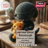 Xenomorph Crochet Emotional Support Plush Toy holding an orange kitten, sitting on a wooden desk near vintage books.