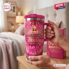 Hand holding a pink Barbie 67th Anniversary Stanley Tumbler with straw inside a bedroom setting.