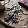 Close-up of a Batmobile keychain with two character figures and a 60th anniversary metal tag on a wooden surface.